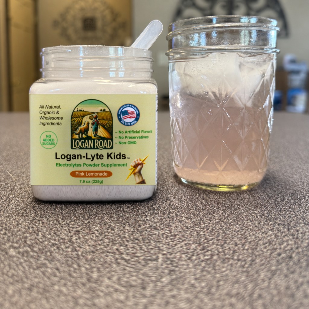 An open jar of Logan-Lyte Kids next to a glass of the pink lemonade drink